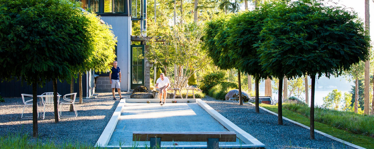 Two men play bocce ball on an oyster shell court in an idyllic setting on a sunny day.